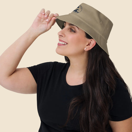 Mujer vistiendo gorro bucket color caqui de estilo vintage con emblema costero.