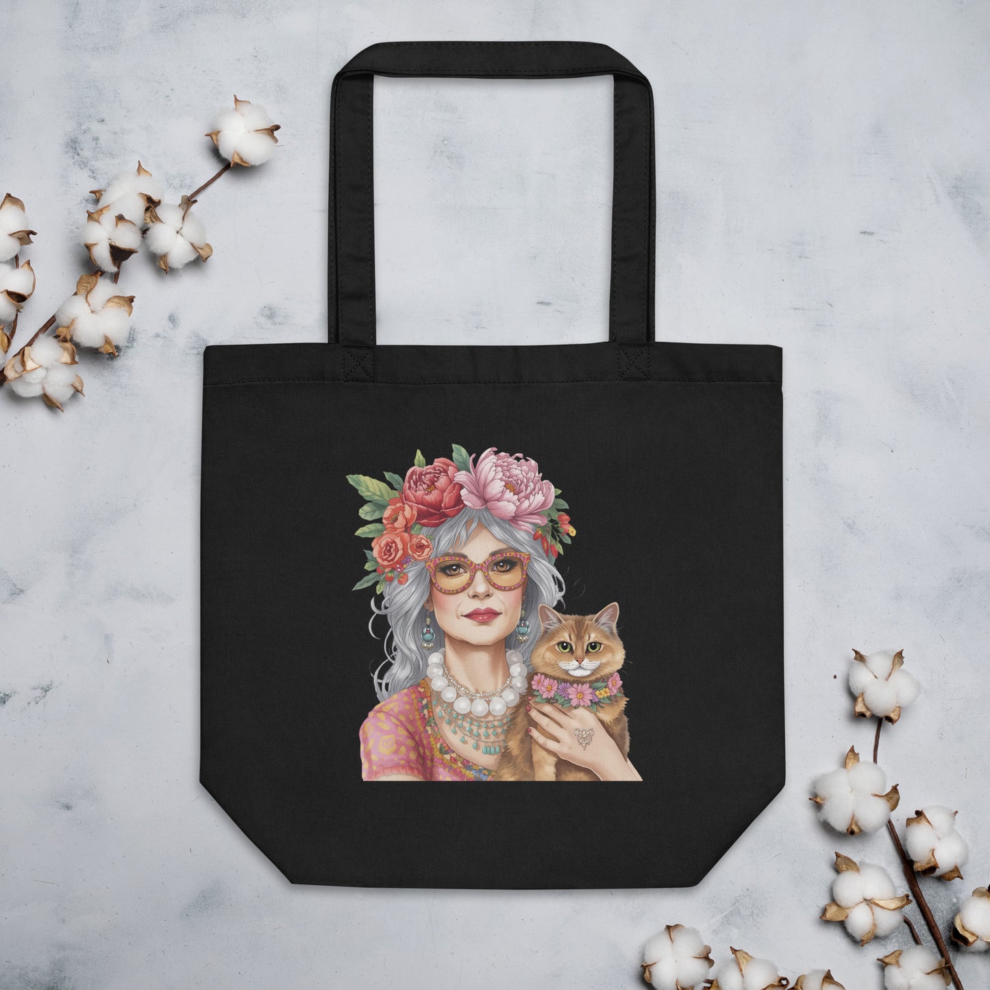 Bolsa de tela negra con ilustración de mujer boho y gato colocada sobre una superficie junto a elementos decorativos
