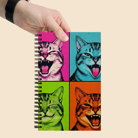 Persona sujetando libreta con diseño de gatos Pop Art coloridos y estética vintage.