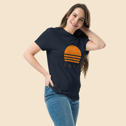 Persona vistiendo camiseta negra con gráfico retro de sol naranja y diseño Sunset 1977.