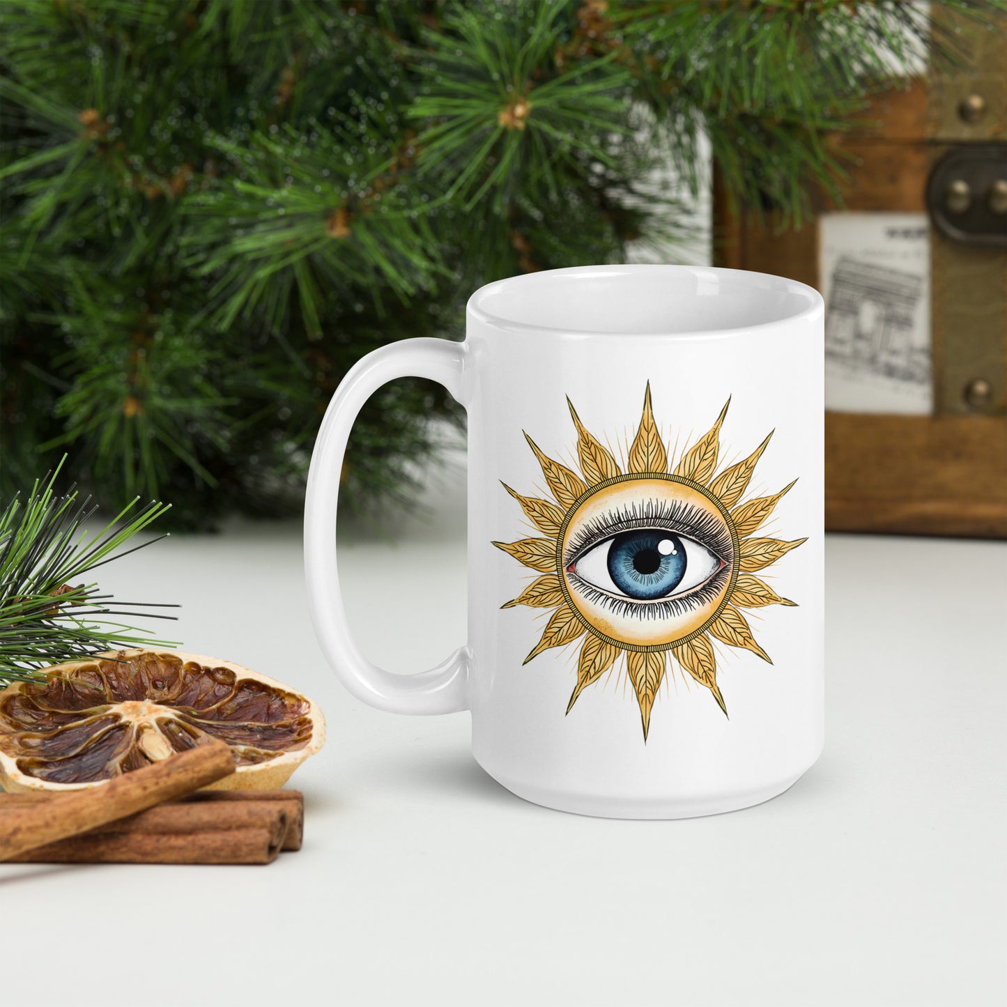 Taza de cerámica blanca con gráfico retro de sol y tercer ojo sobre superficie de madera, acompañada de elementos naturales y botánicos.