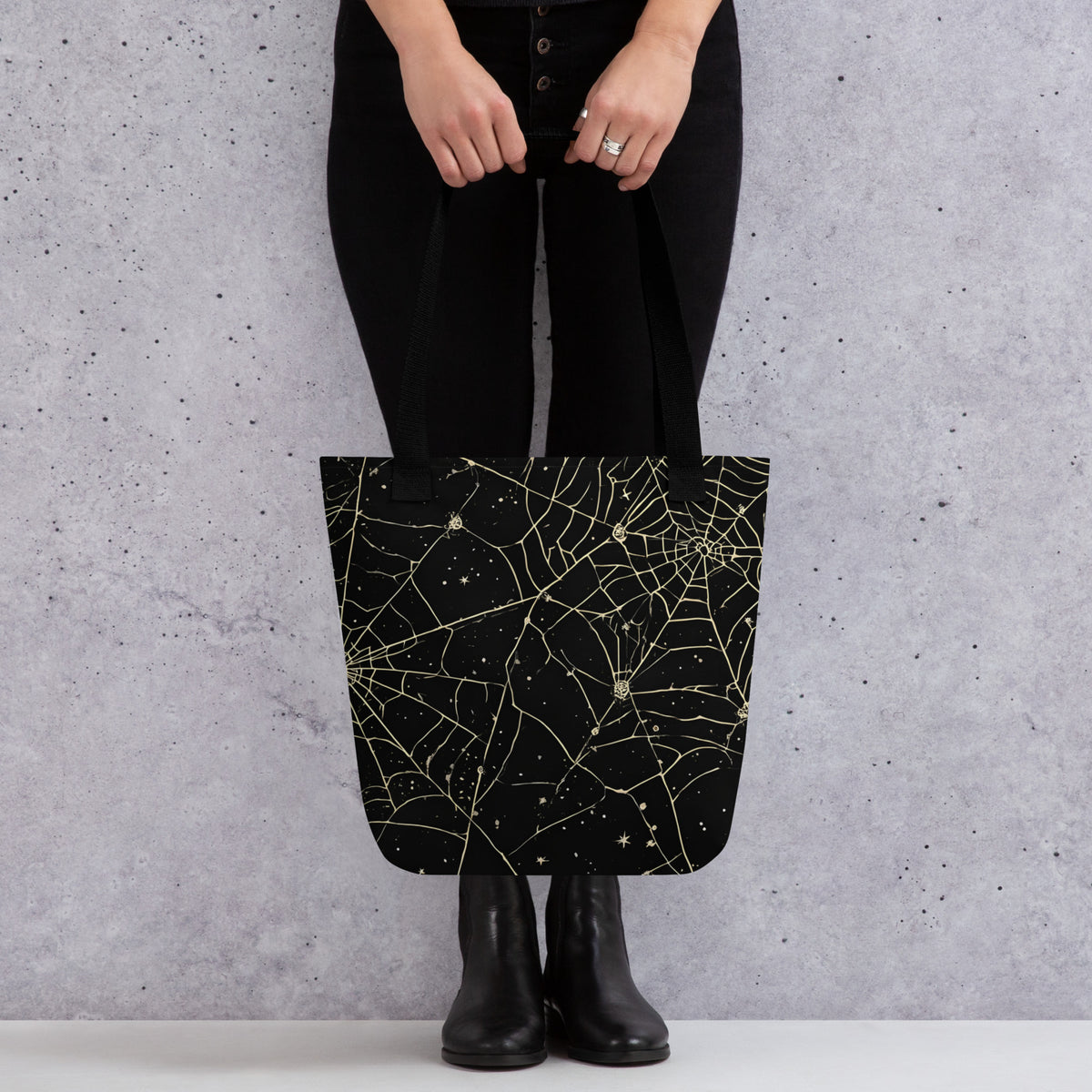 Persona mostrando una bolsa de tela negra con estampado integral de telarañas y motivos de Halloween vintage