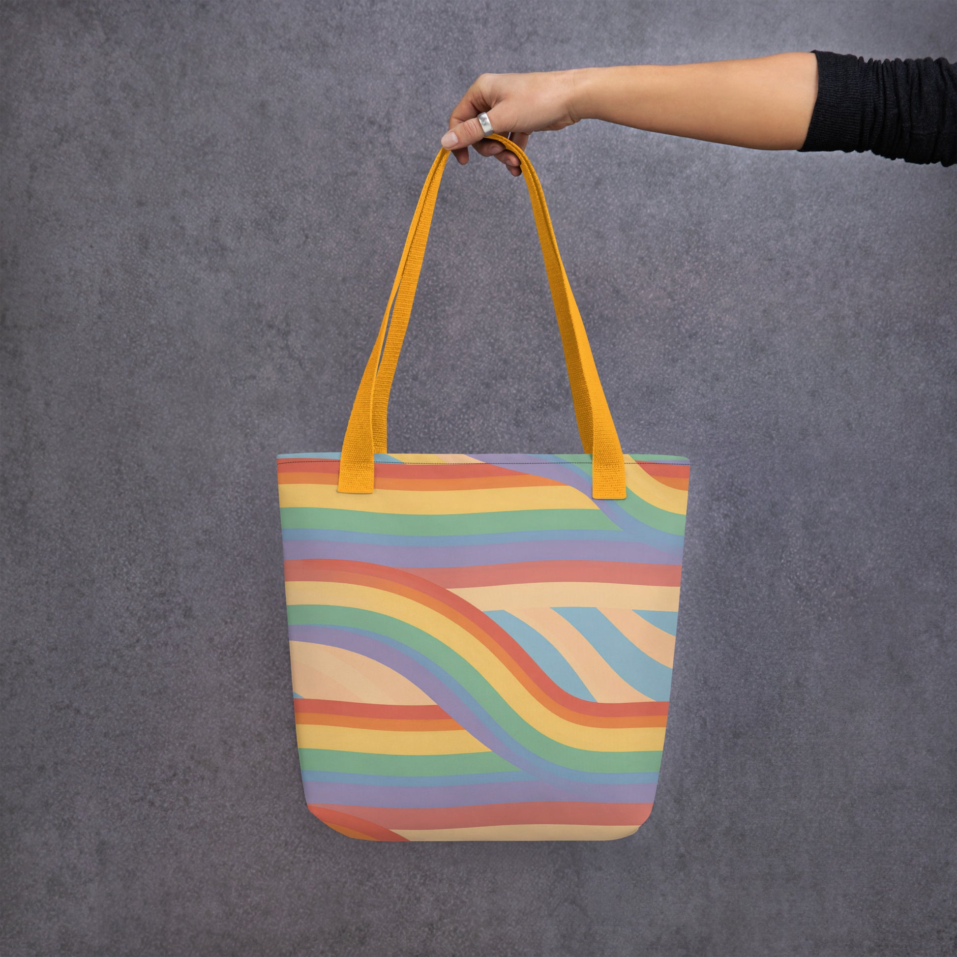 Persona sosteniendo con una mano la bolsa de tela estampada con diseño de ondas Pride vintage sobre fondo oscuro.