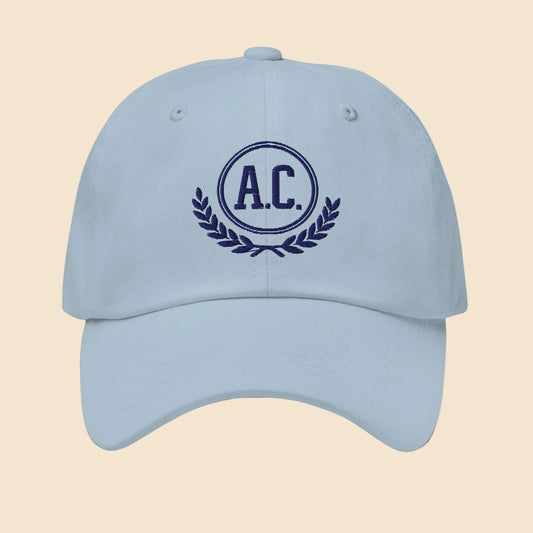 Gorra dad hat unisex en color azul claro con bordado frontal clásico de estilo universitario A.C. y laurel.