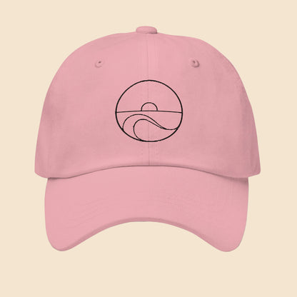 Gorra dad hat de sarga de algodón en color rosa con diseño minimalista bordado de sol y olas del mar en color negro.