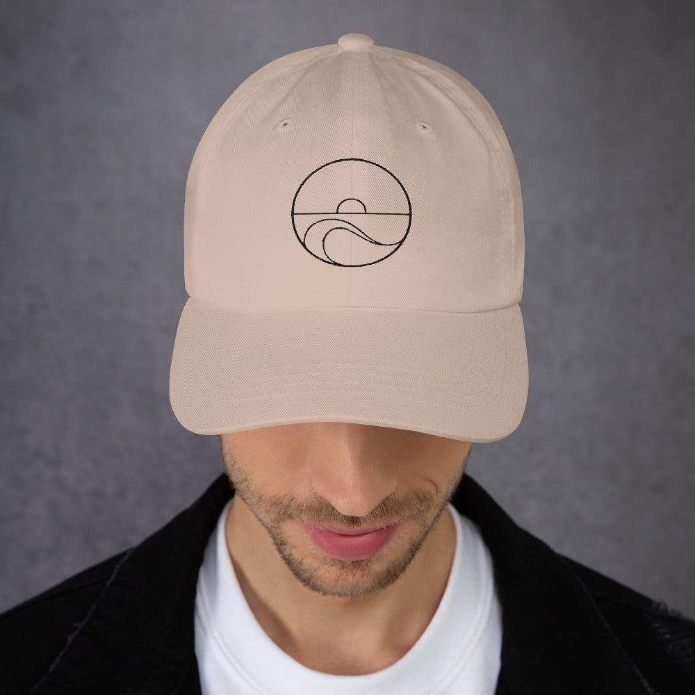 Hombre luciendo la gorra dad hat color piedra con el bordado frontal de sol y mar.
