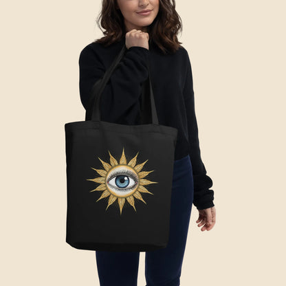 Mujer vistiendo de negro llevando al hombro una bolsa de tela tote bag con ilustración esotérica y bohemia.