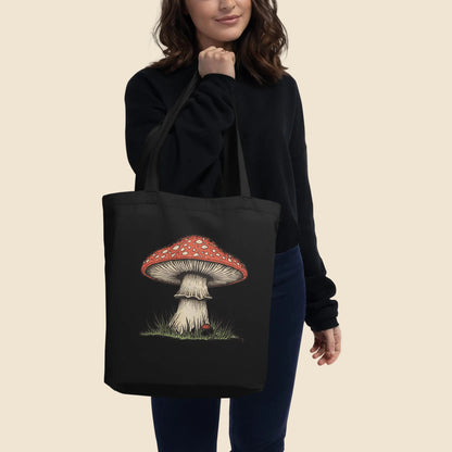 Mujer vistiendo de oscuro llevando al hombro una bolsa de tela tote bag negra con diseño cottagecore silvestre.