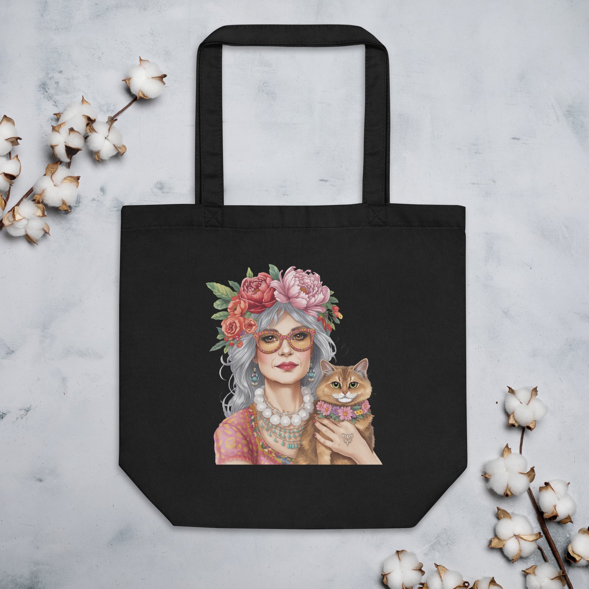 Bolsa de tela negra con ilustración de mujer boho y gato colocada sobre una superficie junto a elementos decorativos