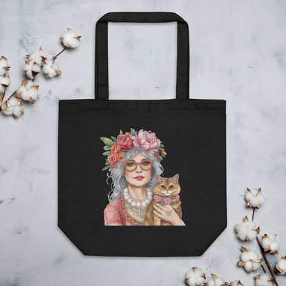 Bolsa de tela negra con ilustración de mujer boho y gato colocada sobre una superficie junto a elementos decorativos