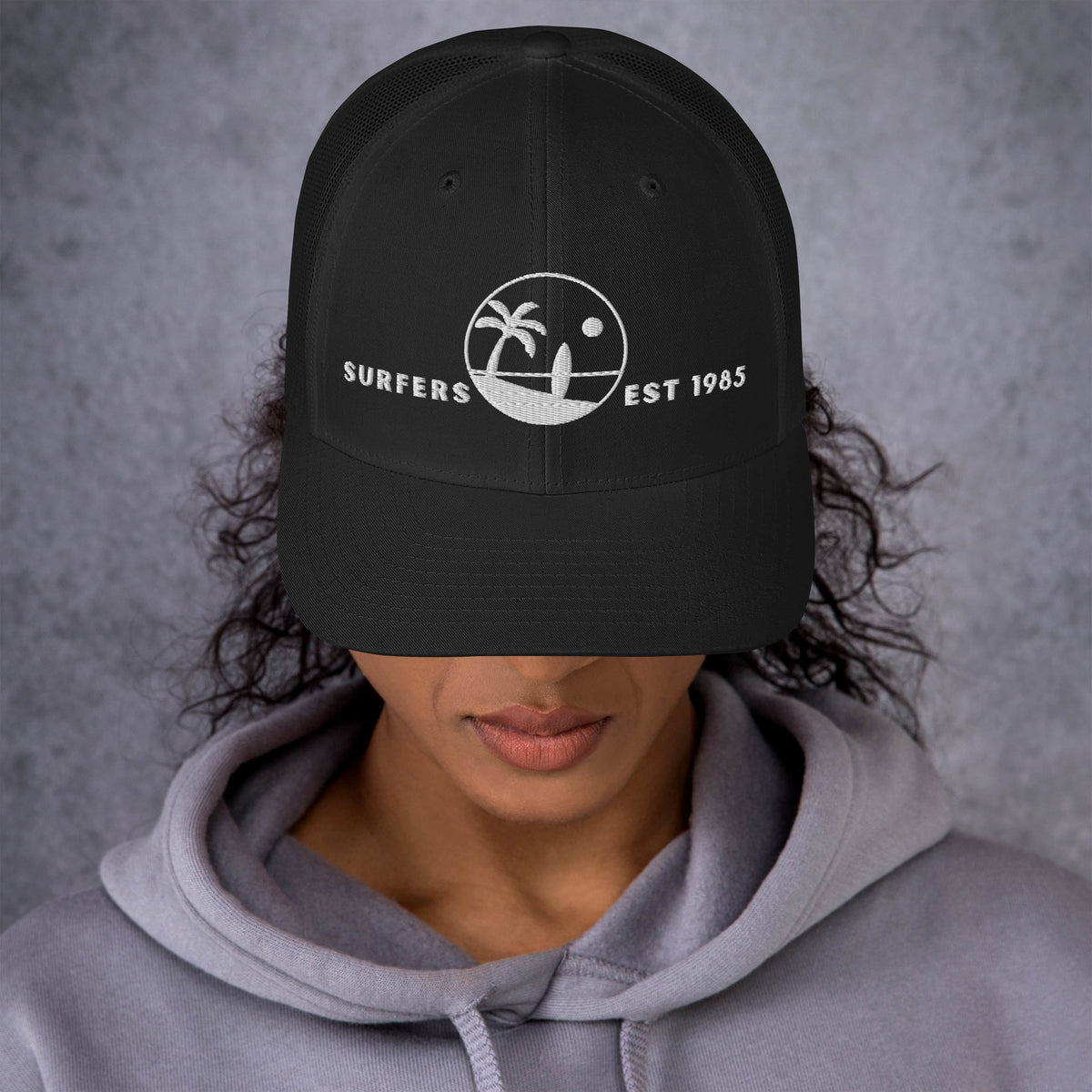 Mujer vistiendo gorra trucker negra estructurada con gráfico de surf de estilo vintage.