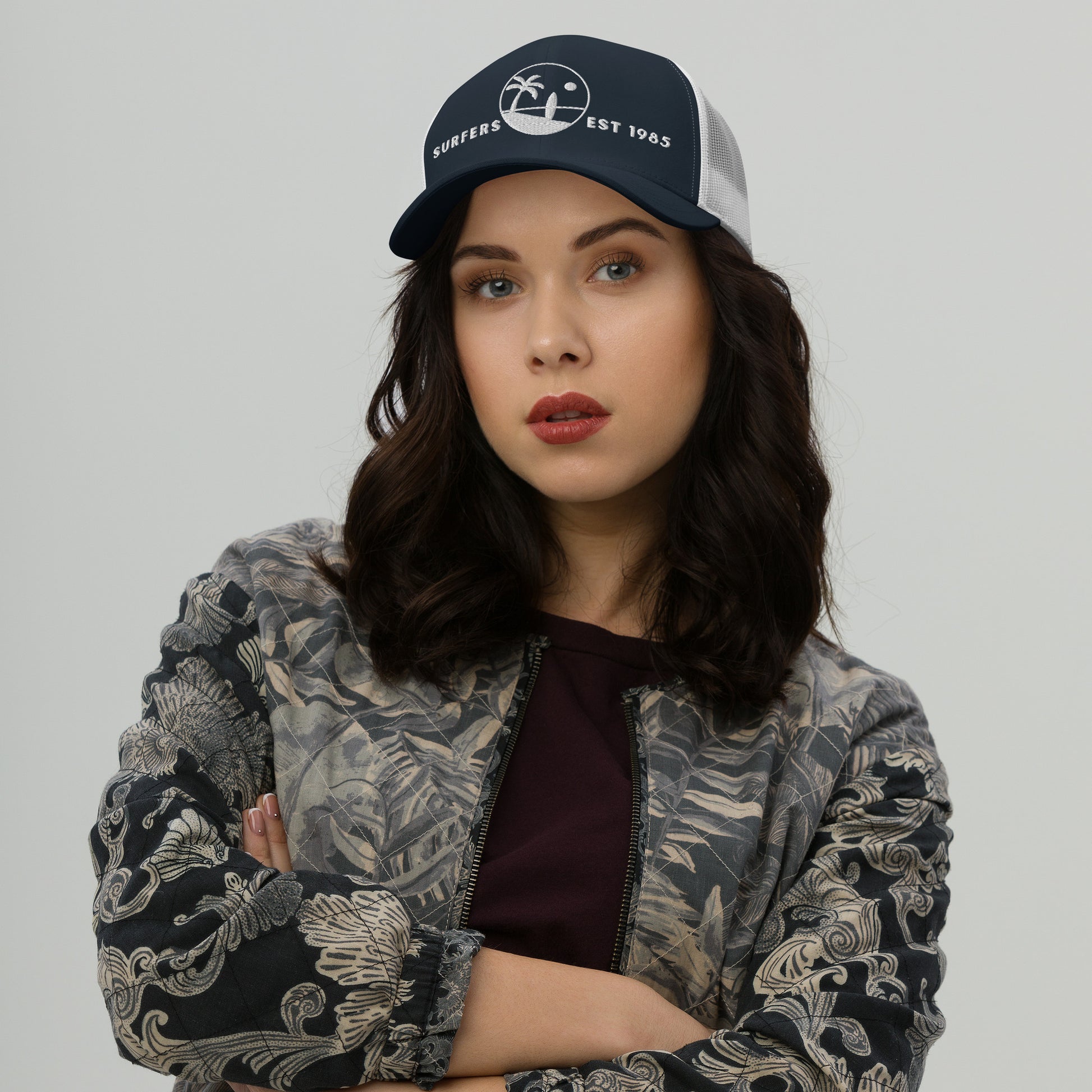 Mujer vistiendo gorra trucker azul marino y blanca con ilustración clásica de palmera y tabla de surf.