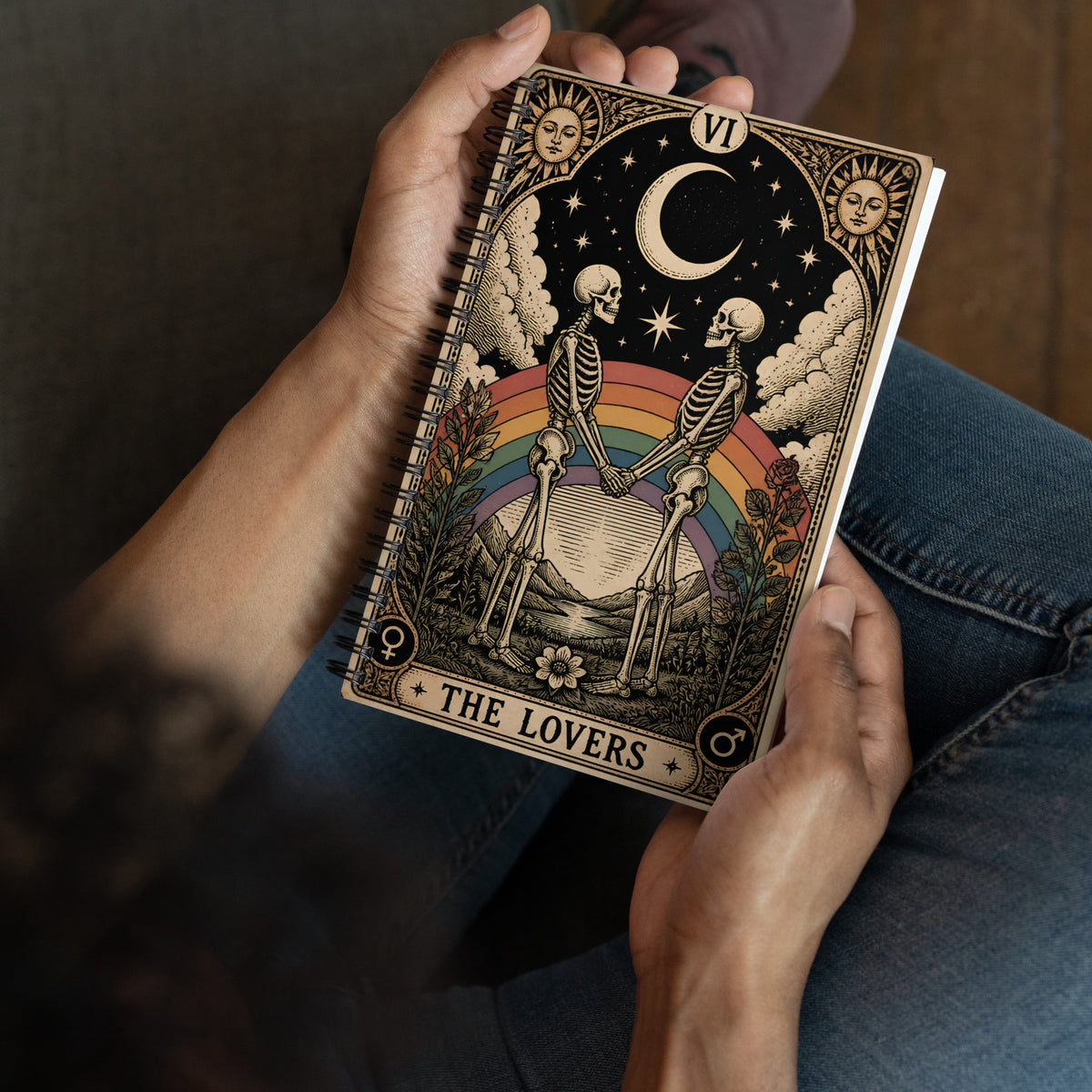 Persona sosteniendo una libreta vintage con diseño de tarot The Lovers y dos esqueletos