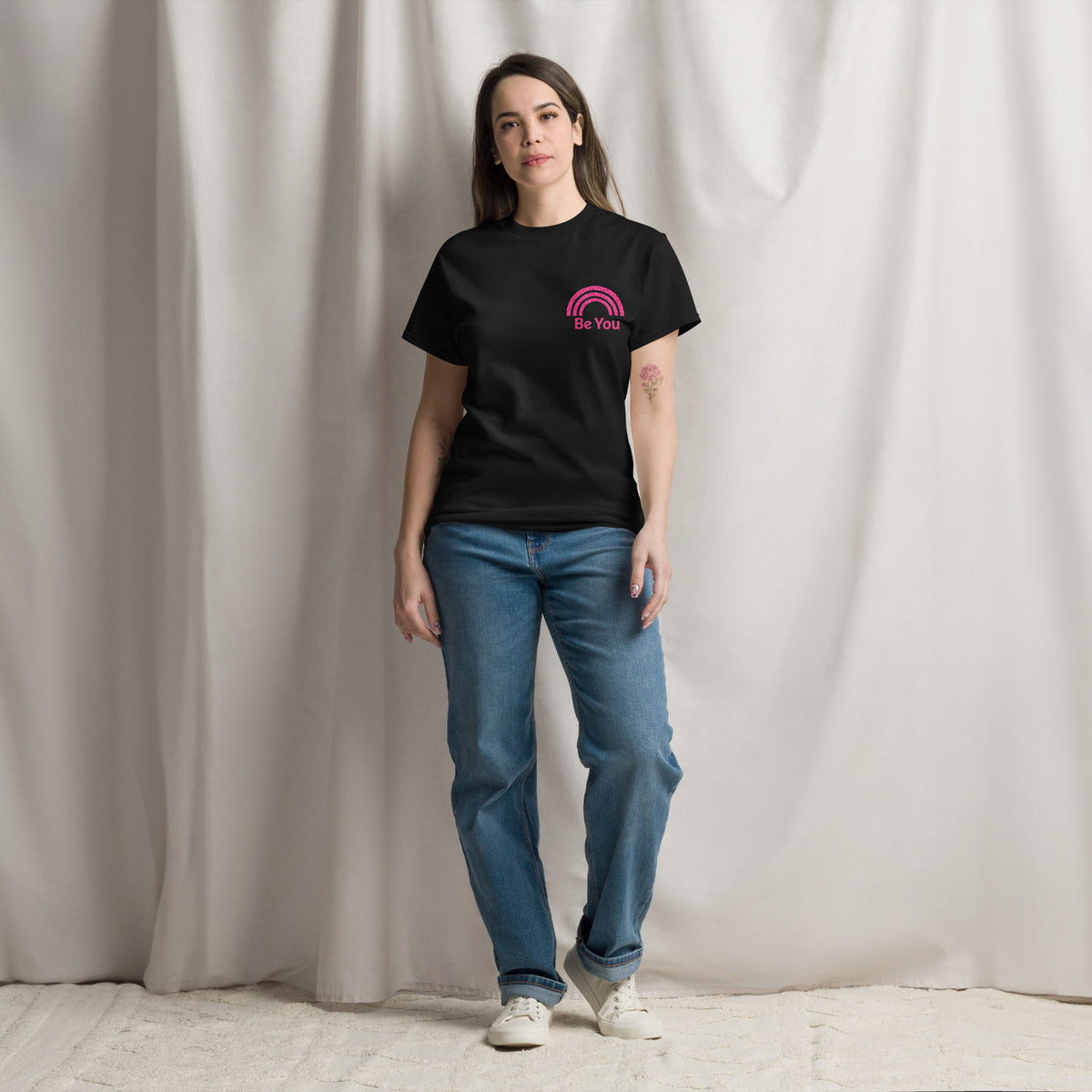 Persona con camiseta negra mostrando diseño Be You con arcoíris rosa.