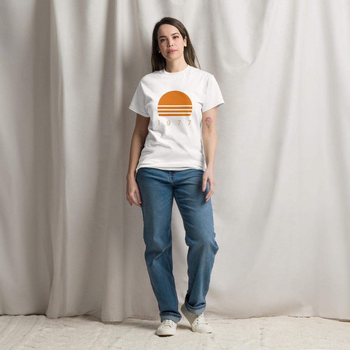 Persona con camiseta blanca mostrando diseño vintage Sunset 1977 de inspiración californiana.