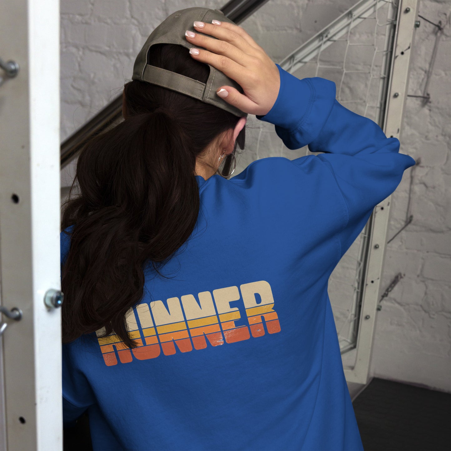 Mujer de espaldas ajustando su sudadera azul royal con tipografía de los años 70.