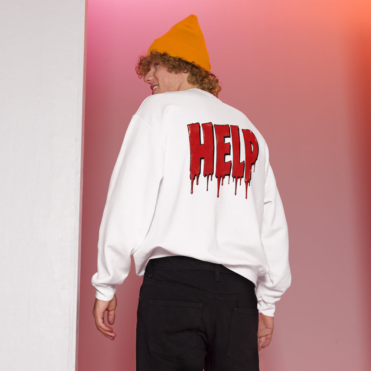 Persona con sudadera blanca HELP y gorro naranja en un fondo rosa
