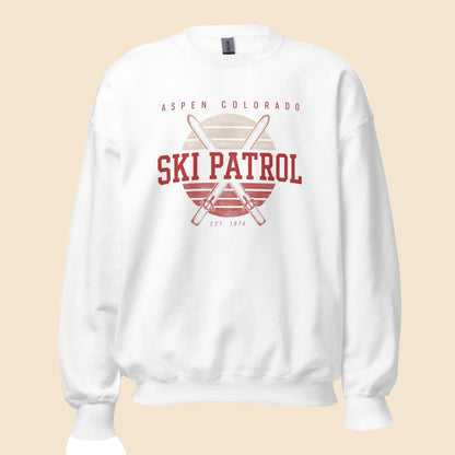 Sudadera unisex de cuello redondo en color blanco con diseño frontal retro Aspen Ski Patrol y esquís cruzados.