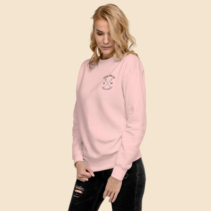 Mujer luciendo sudadera premium rosa pastel con ilustración de remos cruzados.