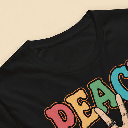 Detalle de camiseta con palabra Peace multicolor y mano haciendo el signo de la paz con estética retro
