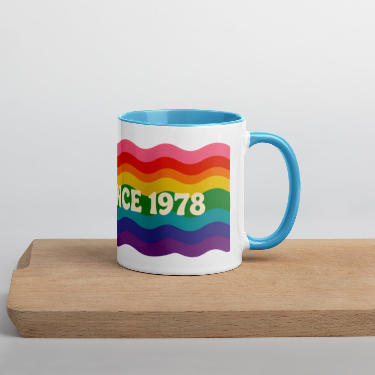 Taza retro Pride de cerámica con mensaje Proud Since 1978 y diseño arcoíris mostrada sobre una superficie de madera.