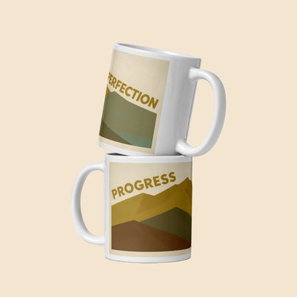 Taza de cerámica blanca brillante con diseño vintage Progress Over Perfection y paisaje de montaña en tonos naturales.