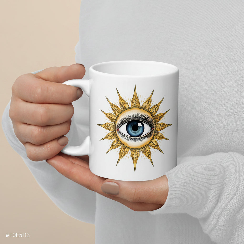 Mano sosteniendo taza de cerámica blanca con diseño vintage de sol dorado y ojo místico azul.