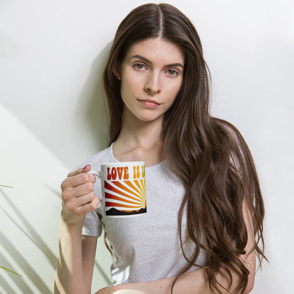 Persona sosteniendo taza blanca Love Is Love con diseño arcoíris vintage inspirado en la estética Pride.