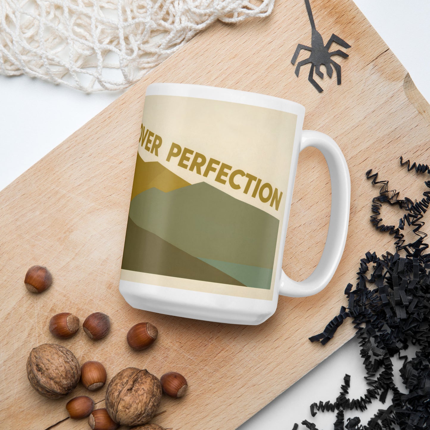 Taza blanca con diseño de montaña vintage junto a granos de café sobre una superficie natural.