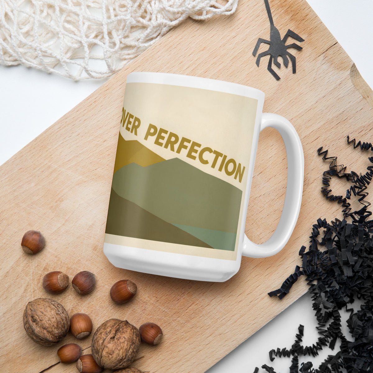 Taza blanca con diseño de montaña vintage junto a granos de café sobre una superficie natural.