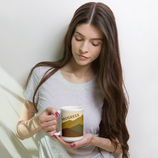 Persona sosteniendo taza blanca de cerámica con mensaje Progress Over Perfection y diseño retro de montaña.